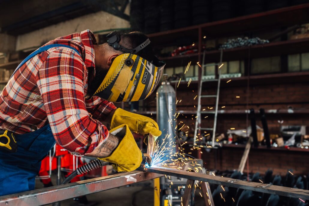 Man in yellow helmet and gloves using a tool to cut through metal