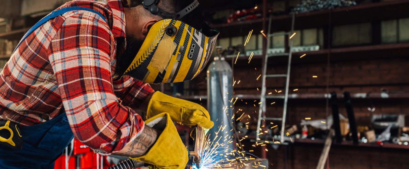 Man in yellow helmet and gloves using a tool to cut through metal